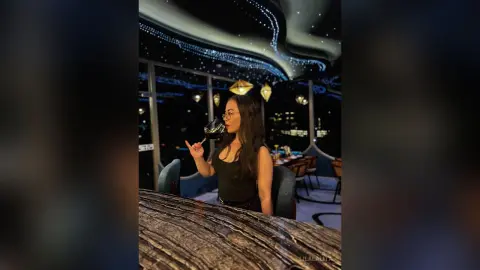 Stylish woman in a black top enjoying a glass of red wine at a luxury rooftop bar with night city views.