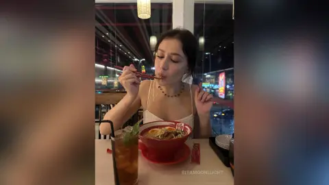 RitaMoonllight eats noodles with red chopsticks, wearing a white lace top while sitting at a restaurant table at night.
