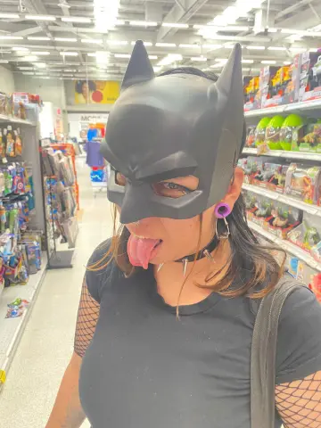 Woman in black t-shirt and Batman mask posing playfully in a grocery store aisle.