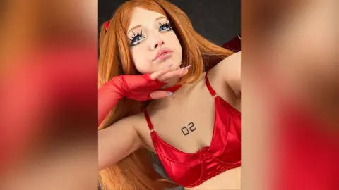 Cosplayer in red lingerie and gloves with long orange hair and dramatic eye makeup posing playfully.