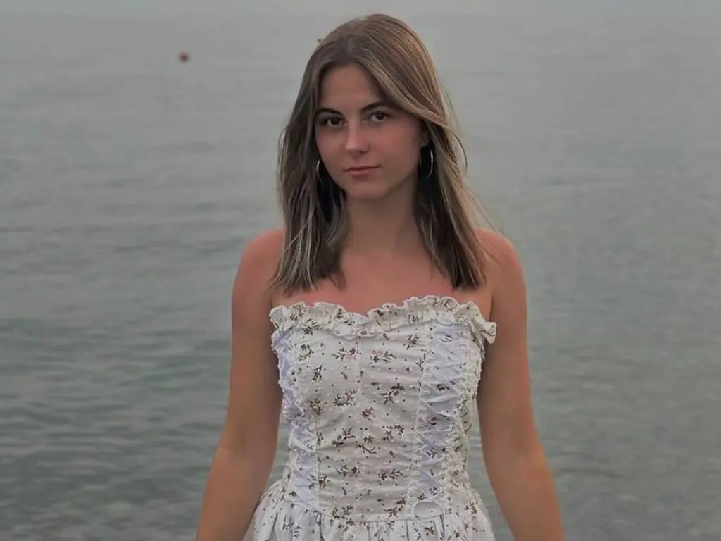 Young woman in a white floral sundress standing by the ocean during a calm sunset.