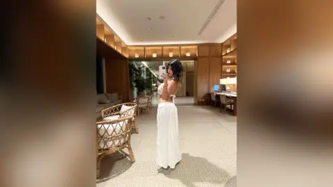 Woman in a white crop top and long skirt taking a mirror selfie in a modern, luxury hotel lounge.
