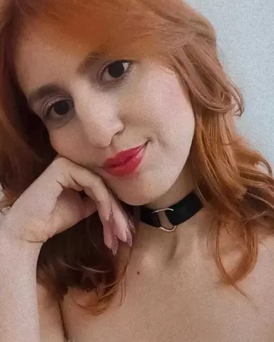 Redheaded woman in a black choker necklace posing with a soft, dreamy expression against a plain background.