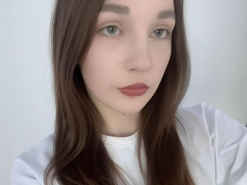 Close-up portrait of a fair-skinned woman with long brown hair and red lipstick wearing a white t-shirt.