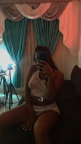 Young woman in a white lace crochet outfit sitting on a sofa in a room with teal curtains.