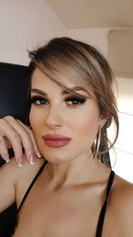Glamorous woman with heavy eyelash makeup and gold hoop earrings posing in a black top.