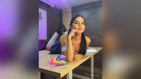 ValeryRouge lies prone on a wooden table wearing a blue plaid skirt and white bra, resting her chin on her hand.