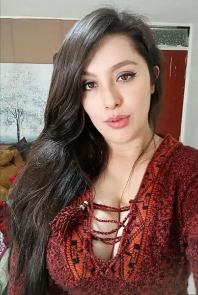 Candelaria_Ferrer poses with long dark hair, wearing a long-sleeved red velvet top that shows cleavage and a hint of her breasts.