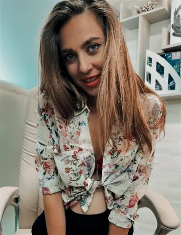 Smiling young woman in a floral print blouse sitting in a bright modern room.