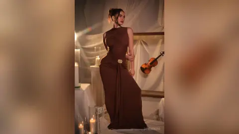 Elegant woman in a brown sleeveless maxi dress posing in a moody, candlelit studio with a violin.