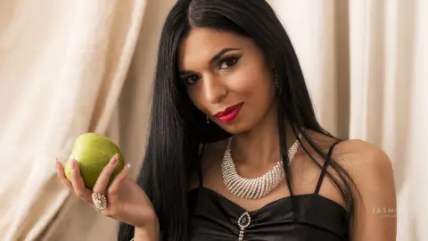 Elegant woman in a black dress holding a green apple against a neutral backdrop with a sophisticated mood.