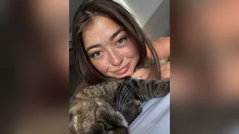 Smiling young woman with nose ring relaxing indoors with a fluffy tabby cat in a cozy mood.