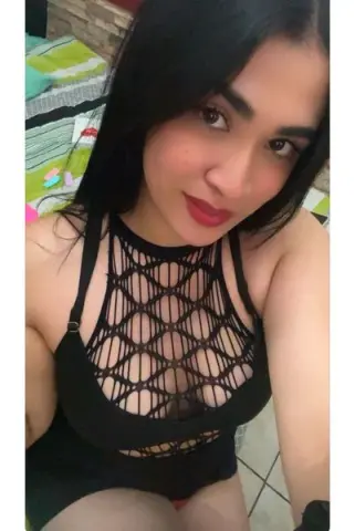 Young woman in a black mesh cutout bodysuit relaxing in a bright indoor setting.