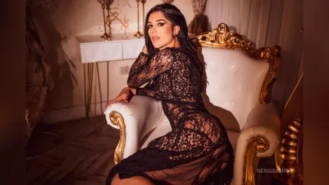 NerissaMist poses in a white and gold chair wearing a sheer black lace dress that shows off her body.
