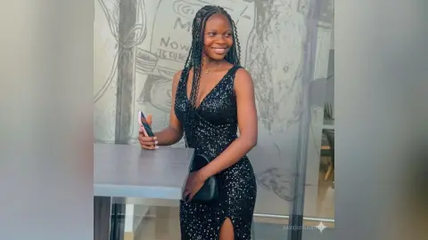 Smiling Black woman in a sparkling black sequin cocktail dress standing by a table in a modern cafe.