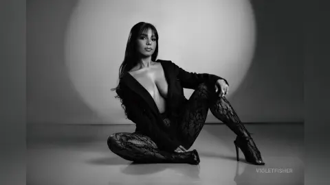 Elegant woman in a black blazer and lace tights posing in a moody black and white studio portrait.