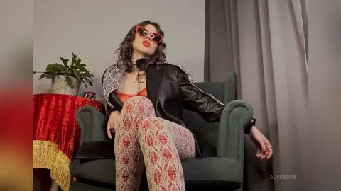 Stylish woman in patterned tights and black leather jacket sitting in a vintage armchair with a retro mood.