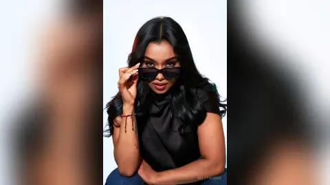 Stylish woman in a black top and sunglasses posing confidently against a white background.