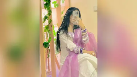 Young woman in elegant white and purple traditional Indian ethnic wear taking a mirror selfie in a bright room.