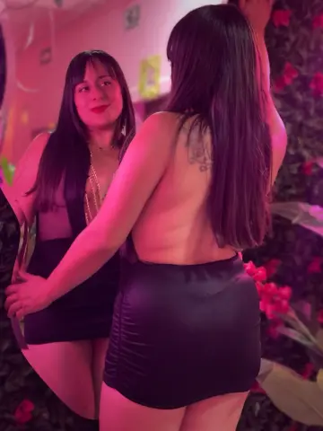 Young woman in a black mini dress posing in a moody, pink-lit nightclub setting.