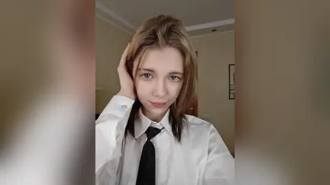 Young woman in a white button-down shirt and black tie posing with a soft expression in a bright room.