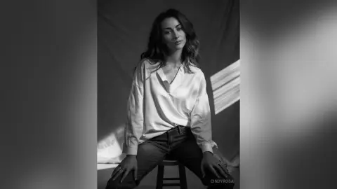 Elegant woman in a white silk blouse and jeans posing in moody studio lighting.