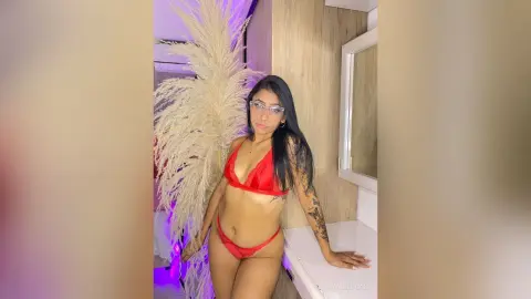 Young woman in a red bikini posing in a modern room with decorative pampas grass decor.