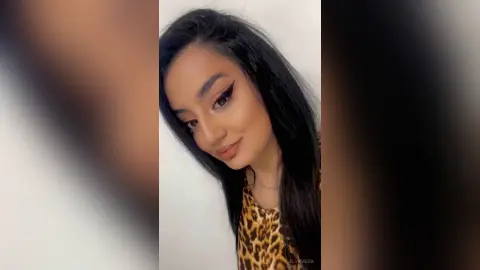 Young woman with winged eyeliner and leopard print top smiling in a bright indoor setting.