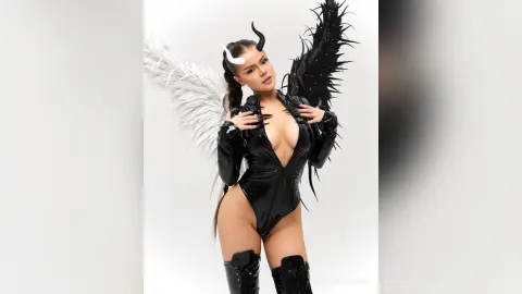 Woman in black latex bodysuit with large white and black angel wings posing in a studio setting.
