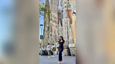 Stylish woman in a black evening dress posing in front of the Sagrada Familia cathedral in Barcelona.