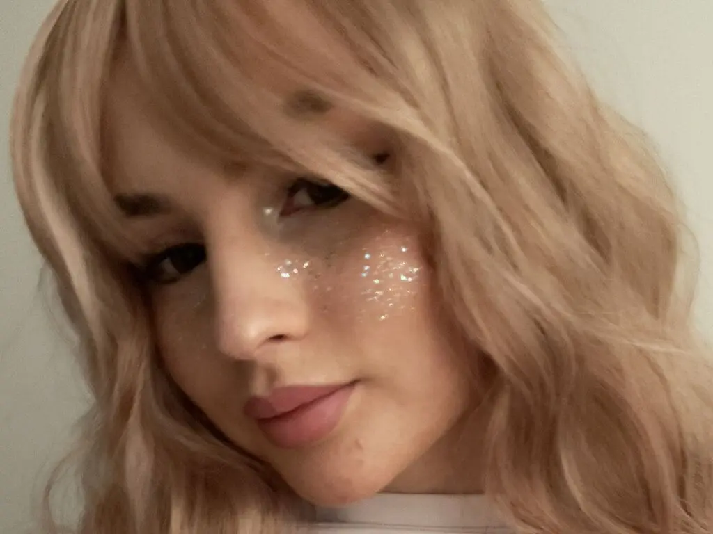 Close-up portrait of a blonde woman with glitter makeup and a soft, dreamy aesthetic.