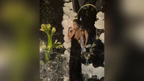 Elegant woman in a black sequin evening gown posing in a glamorous disco-themed party setting with silver decor.