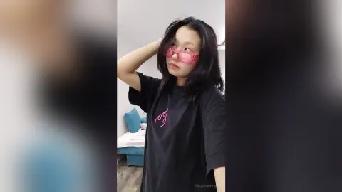 TishaOyervides wearing a black t-shirt and pink glasses while running her hand through her long black hair.