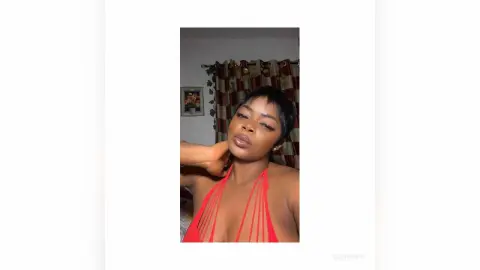 Glamorous woman in a red halter top posing in a cozy indoor setting with a confident mood.