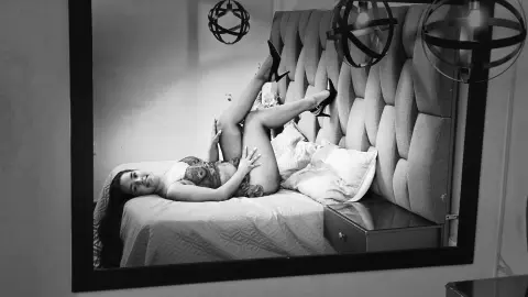 Glamorous woman in lace lingerie relaxing on a bed in a moody, black and white bedroom setting.