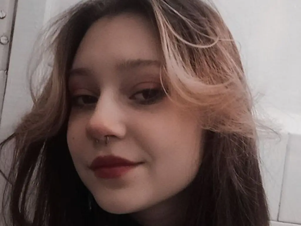 Close-up portrait of a young woman with wavy brown hair and red lipstick in a soft, moody indoor setting.