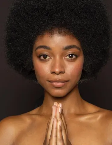 Serene Black woman with natural afro hair posing with hands together in a moody studio portrait.