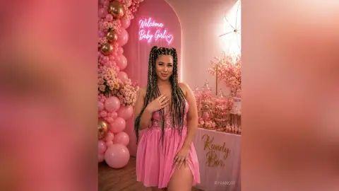 Smiling woman in a pink dress at a dreamy pink baby girl welcome party with balloon decor and a candy bar.