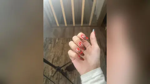Close-up of a hand with trendy red and black swirl pattern nail art design in a modern indoor setting.