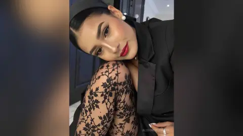 Elegant woman in a black blazer and lace patterned leggings posing with glamorous makeup and red lipstick.