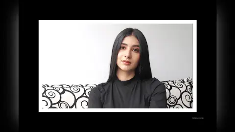 Young woman with long dark hair wearing a black turtleneck sitting against a white background.