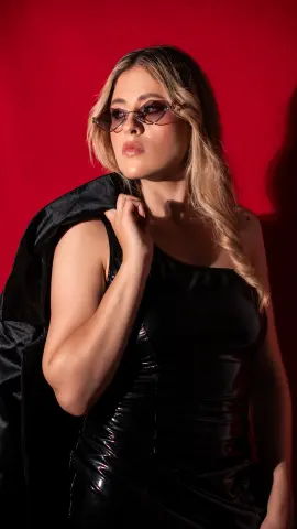 Stylish woman in a black satin dress and sunglasses posing against a bold red background.
