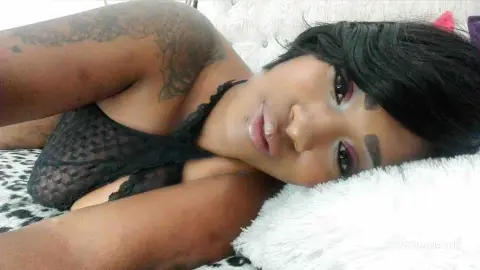 Tattooed woman in a black lace bodysuit relaxing on a white fuzzy pillow with a soft, dreamy mood.