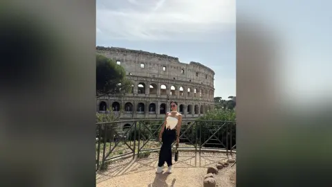 Stylish woman in a white top and black trousers posing in front of the historic Roman Colosseum under a clear sky.