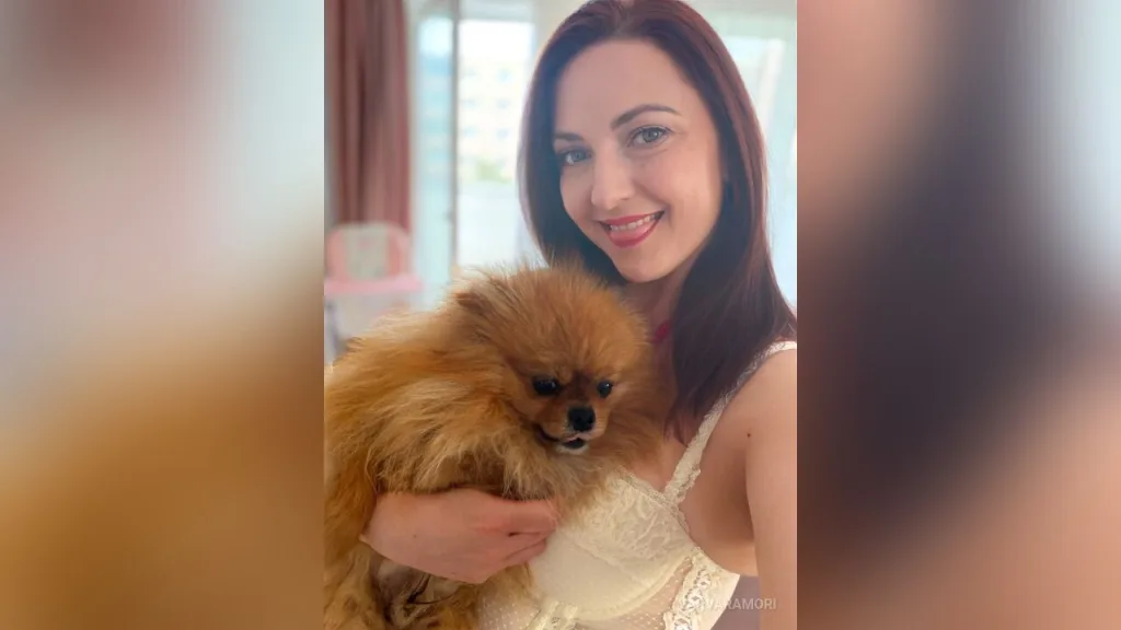 VarvaraMori — VarvaraMori smiles while holding a small brown Pomeranian dog in a white lace top.