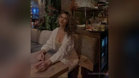Young woman in a white blouse sitting at a restaurant table in a moody, dimly lit cafe setting.