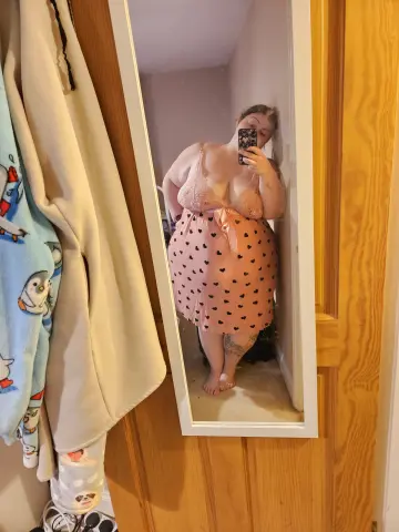 CurvesWithBBW takes a mirror selfie wearing a pink heart-patterned slip dress and lace bra.