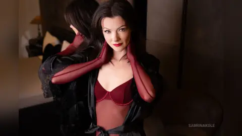 SabrinaKole poses in a black lace robe and red lingerie, looking at the camera with dark hair and red lipstick.