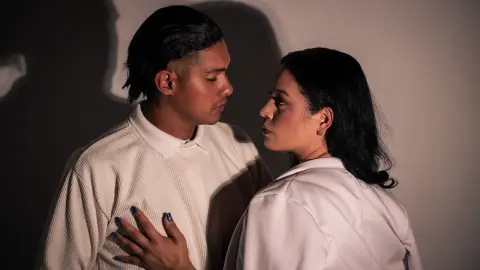Romantic couple in white outfits sharing an intimate moment against a dark studio background.