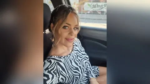 Smiling woman in a black and white zebra print top sitting in a car on a sunny day.